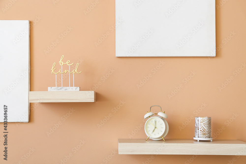 Shelves with alarm clock and decor hanging on color wall