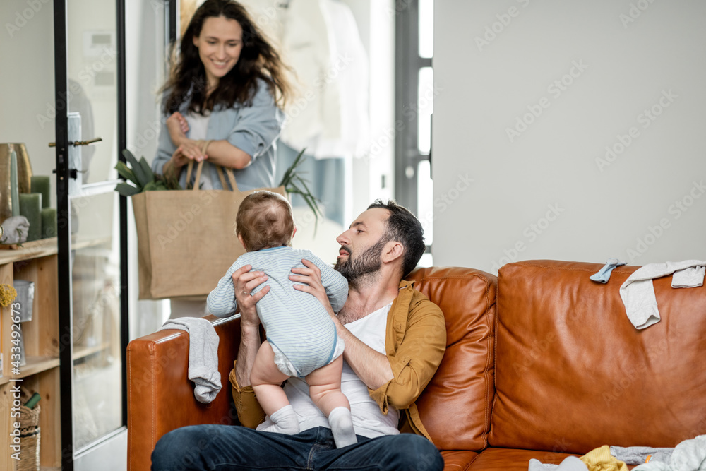 Middle aged dad carrying and playing with newborn baby at home while mom return from shopping. Paren