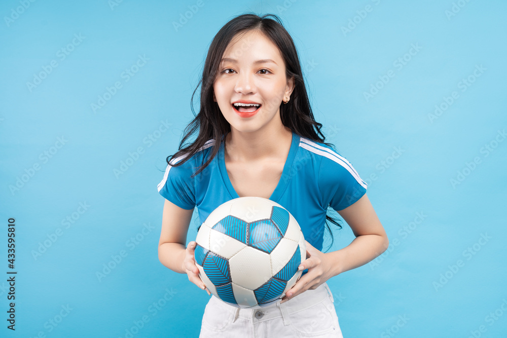 Beautiful Asian woman posing with soccer ball on blue background