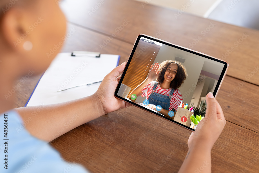 Mixed race businesswoman sitting at desk using tablet having video call with female colleague