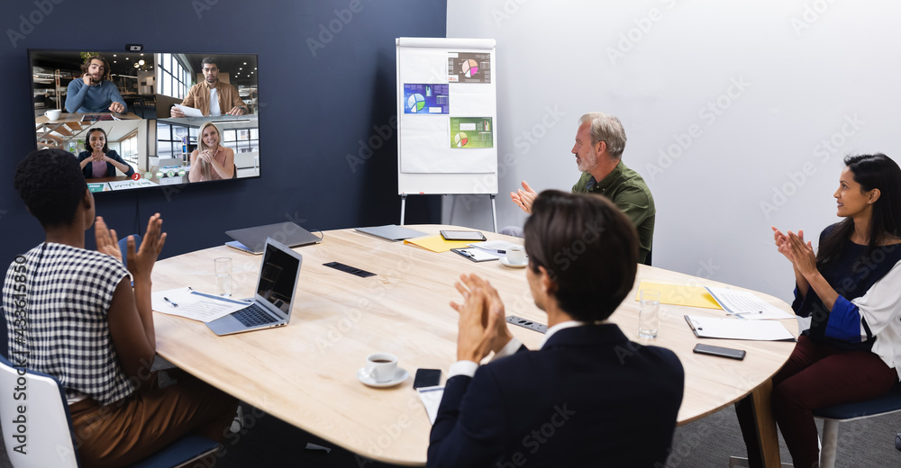 Diverse group of business colleagues having video call with coworkers on screen in meeting room