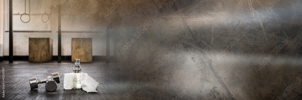 Composition of dumbbells, towel and water bottle on gym floor with blurred grey light