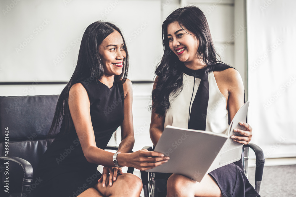 Two businesswomen discussing business while looking at financial data in their hands. They are sitti