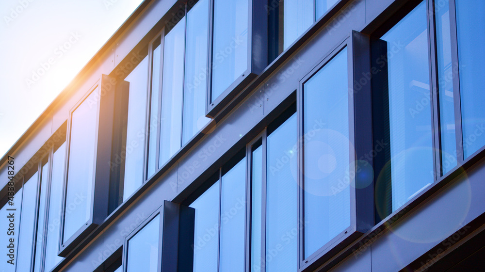 Modern glass building and rising sun. Glass facade on a bright sunny day with sunbeams in the blue s