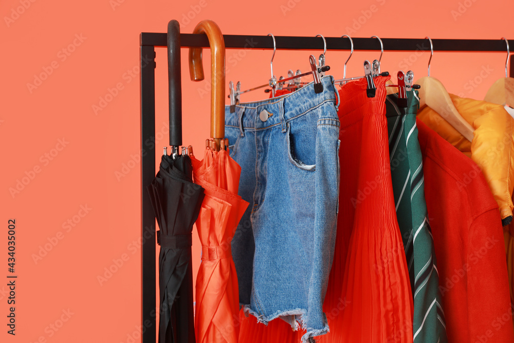 Rack with stylish clothes and umbrellas on color background