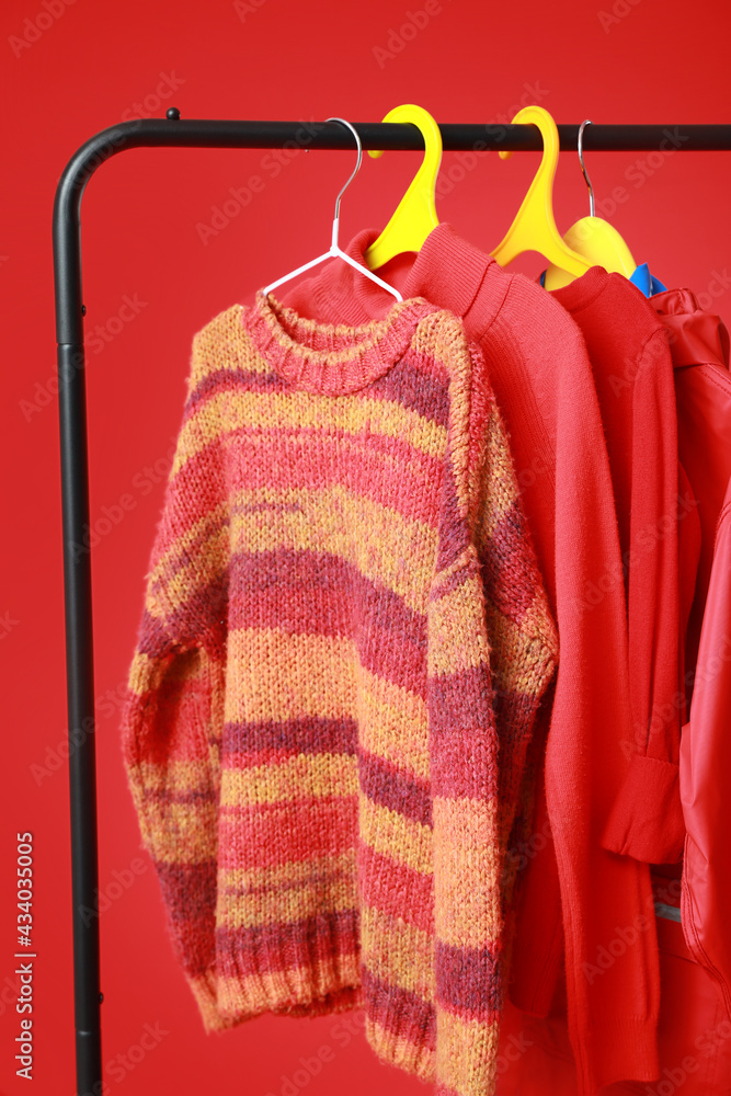 Rack with stylish clothes on color background