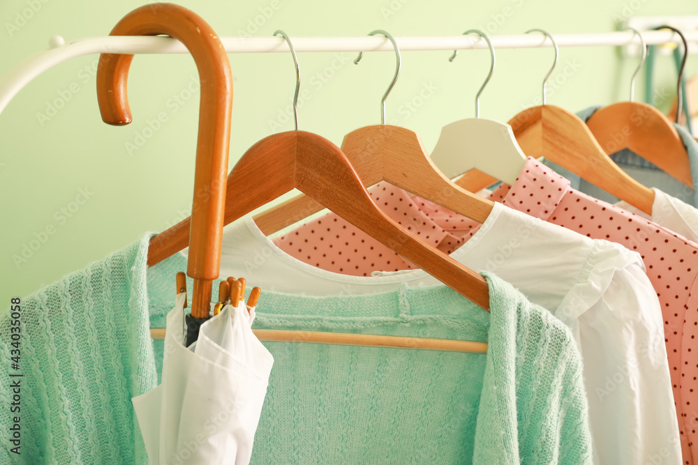 Rack with stylish clothes and umbrella near color wall, closeup