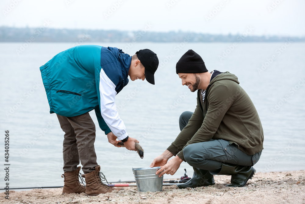 Happy father and son with caught fish on river bank