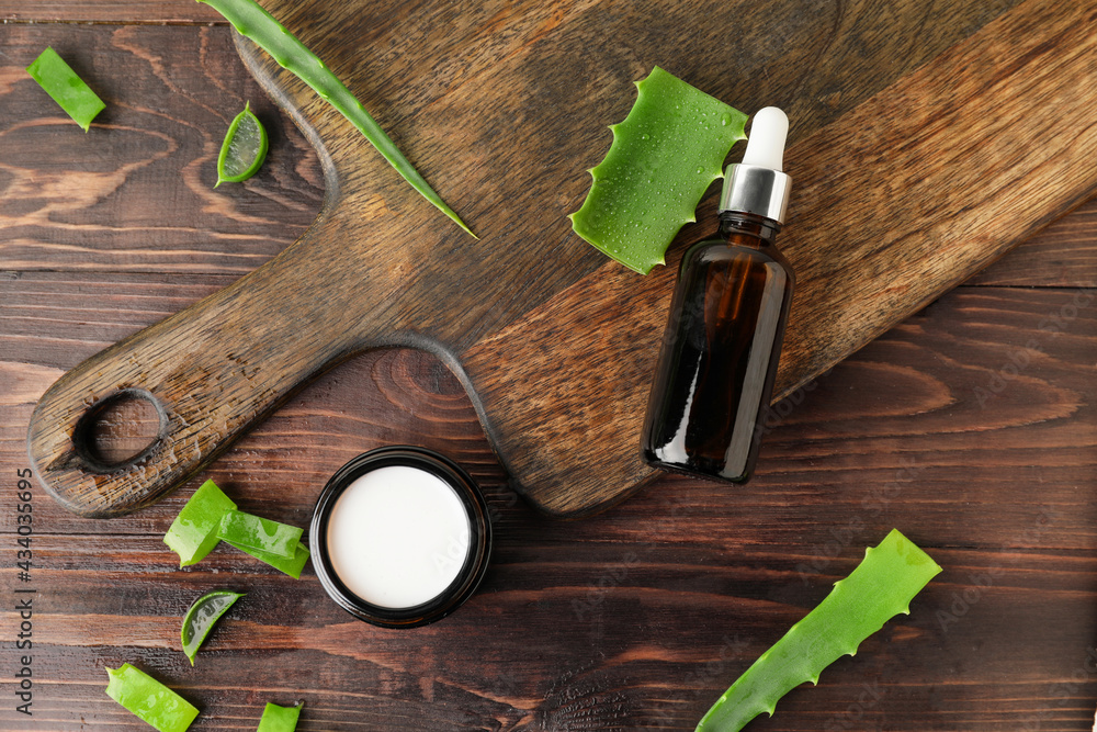 Jar with cream, bottle of essential oil and aloe pieces on wooden background