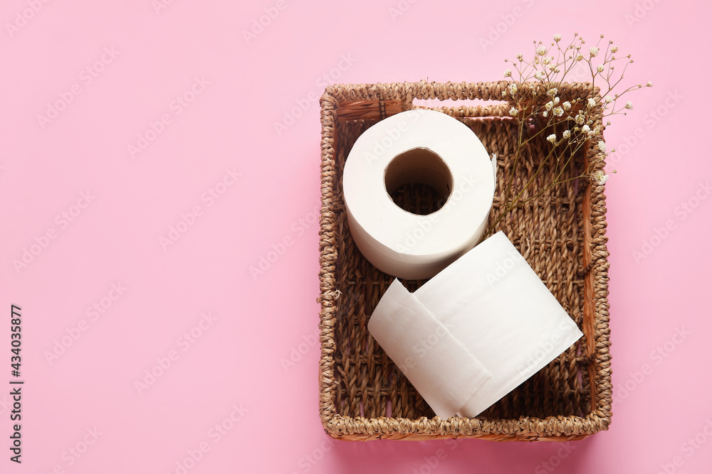 Basket with rolls of toilet paper and flowers on color background