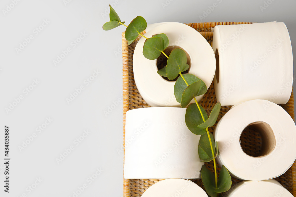 Basket with rolls of toilet paper and eucalyptus on grey background, closeup