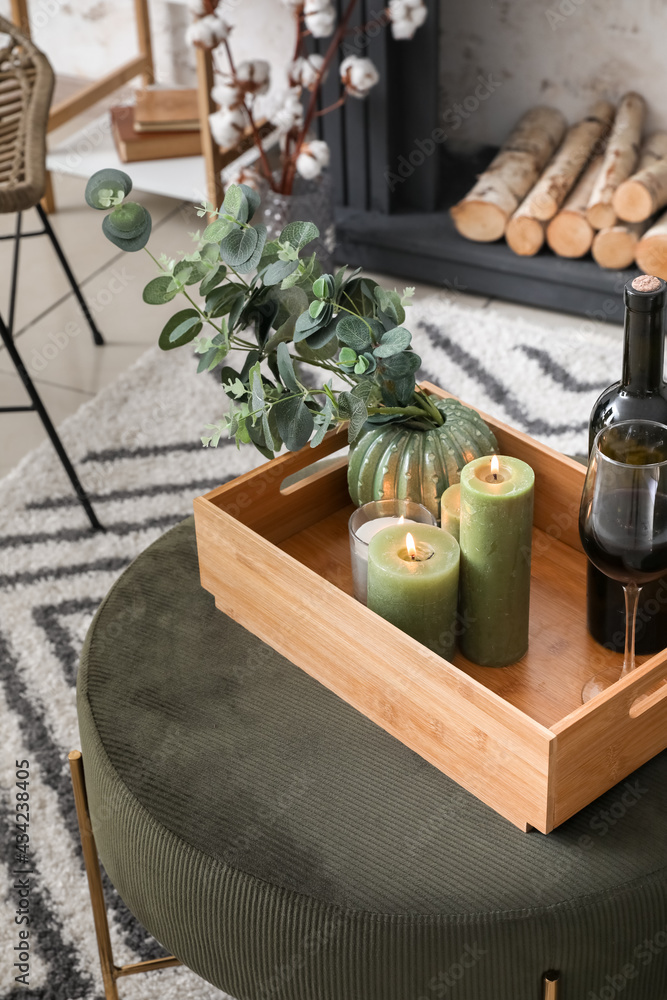 Tray with burning candles and wine on pouf in room