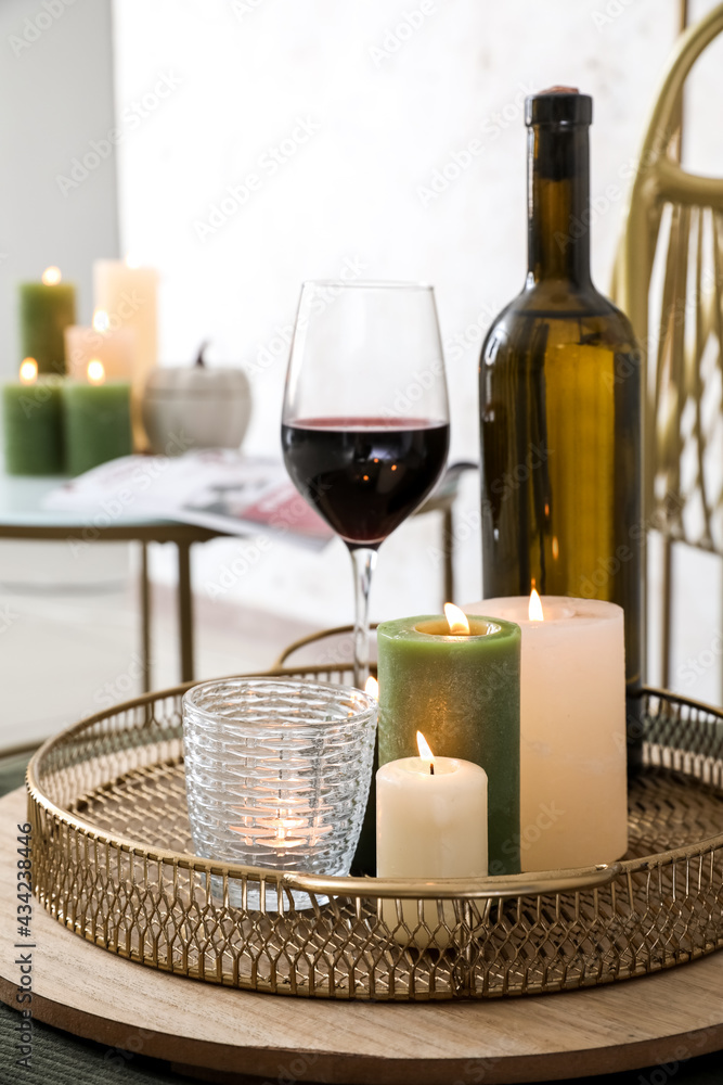 Tray with burning candles and wine on table in room, closeup