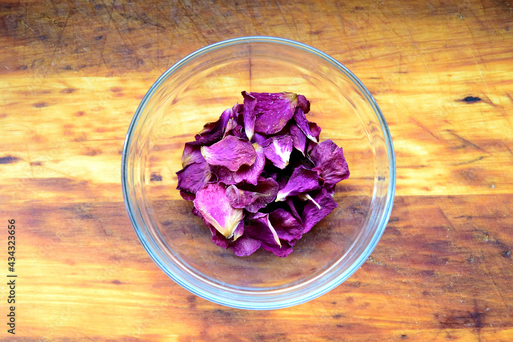 purple rose petals in glass bowl on wooden table - close up