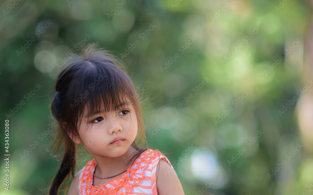 A little adorable Asian girl with sad eyes walking in the park alone.