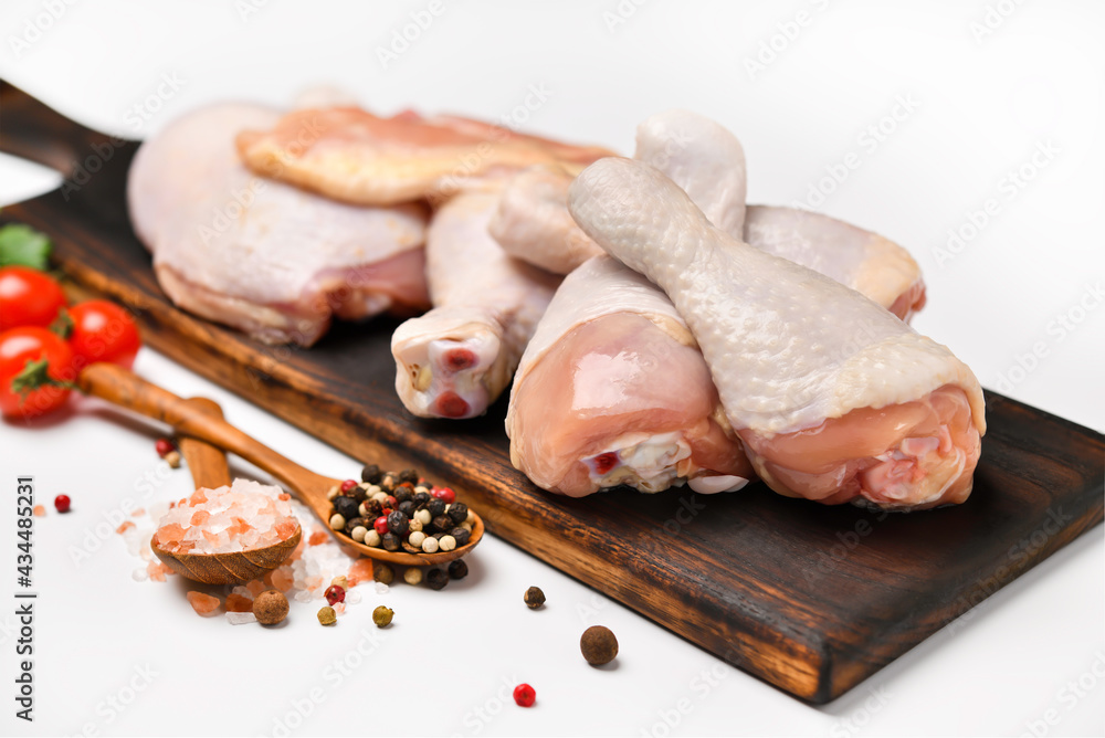 Fresh raw chicken thighs with ingredients for cooking on a wooden cutting board on white background