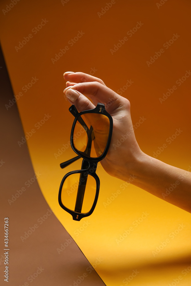 Female hand with stylish sunglasses on colorful background