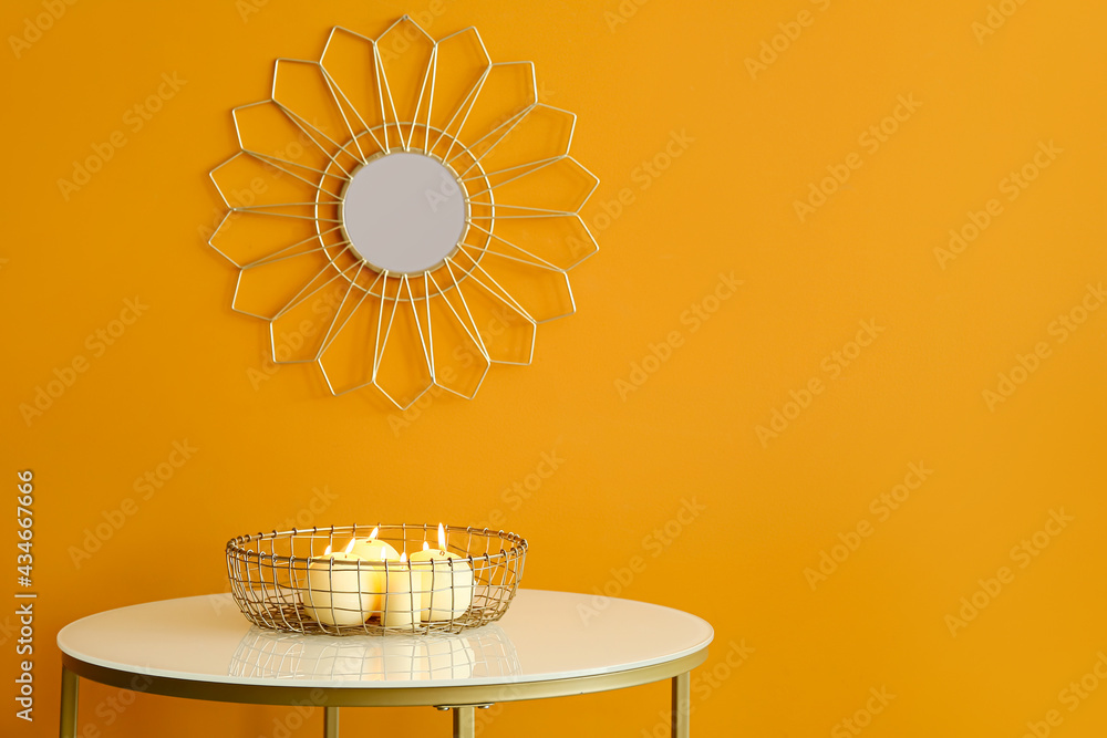 Tray with burning candles on table near color wall