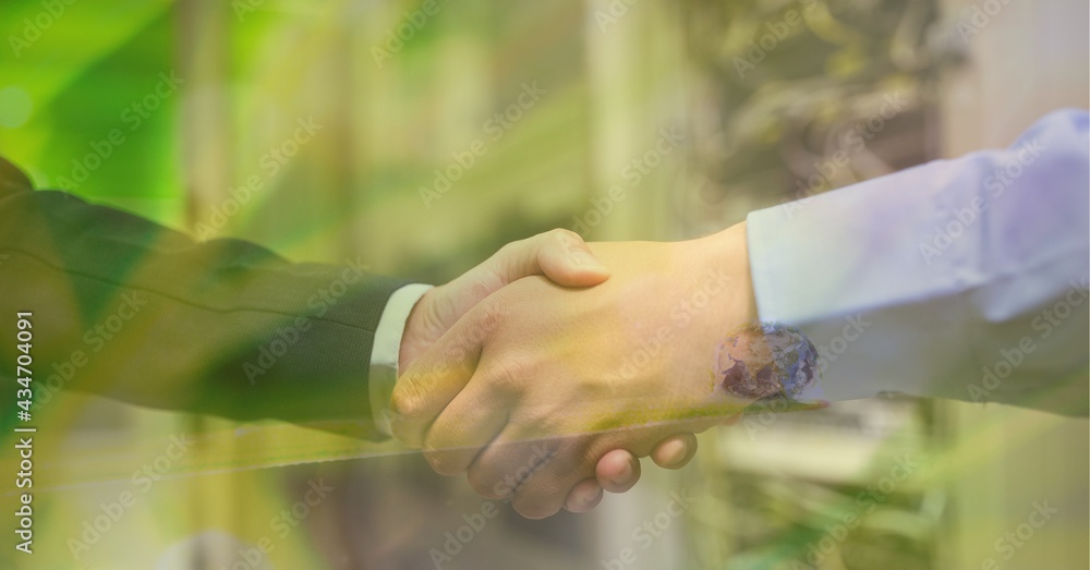 Digital composite image of trees against mid section of two businessmen shaking hands