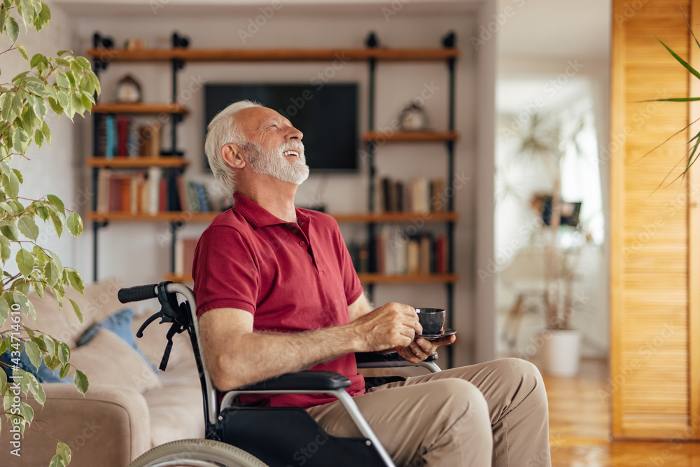 Mature man in a wheelchair, holding cup of coffee, while laughing.