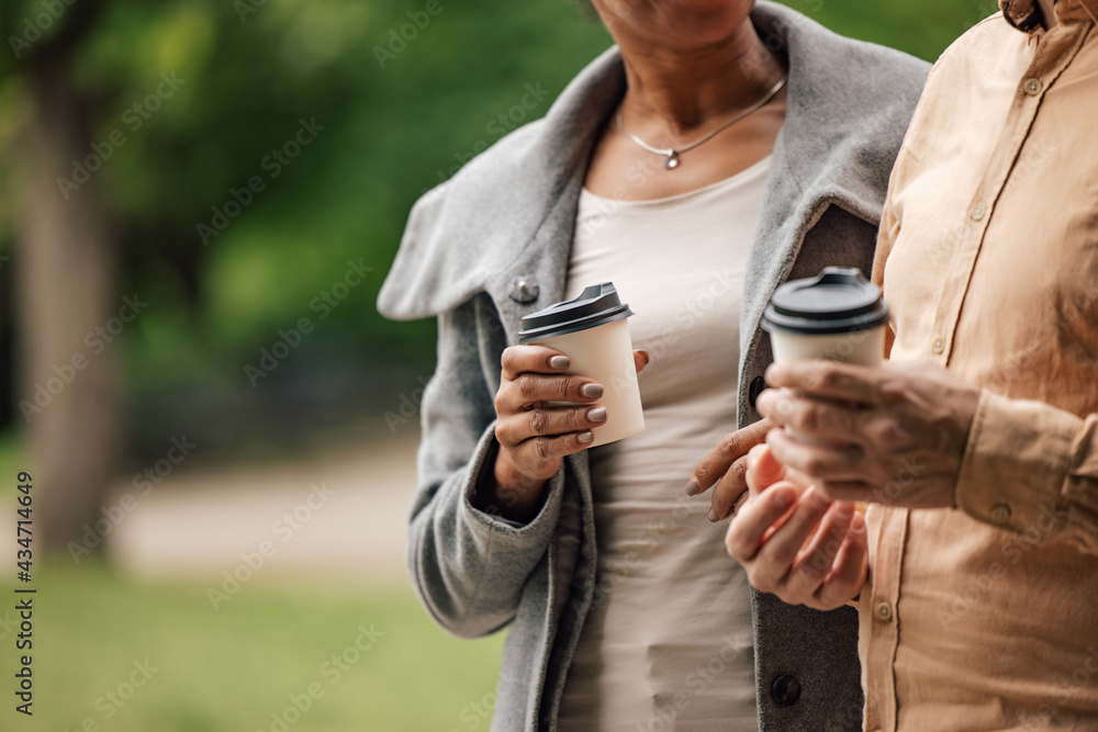 成年情侣拿着外卖咖啡杯，走在外面。