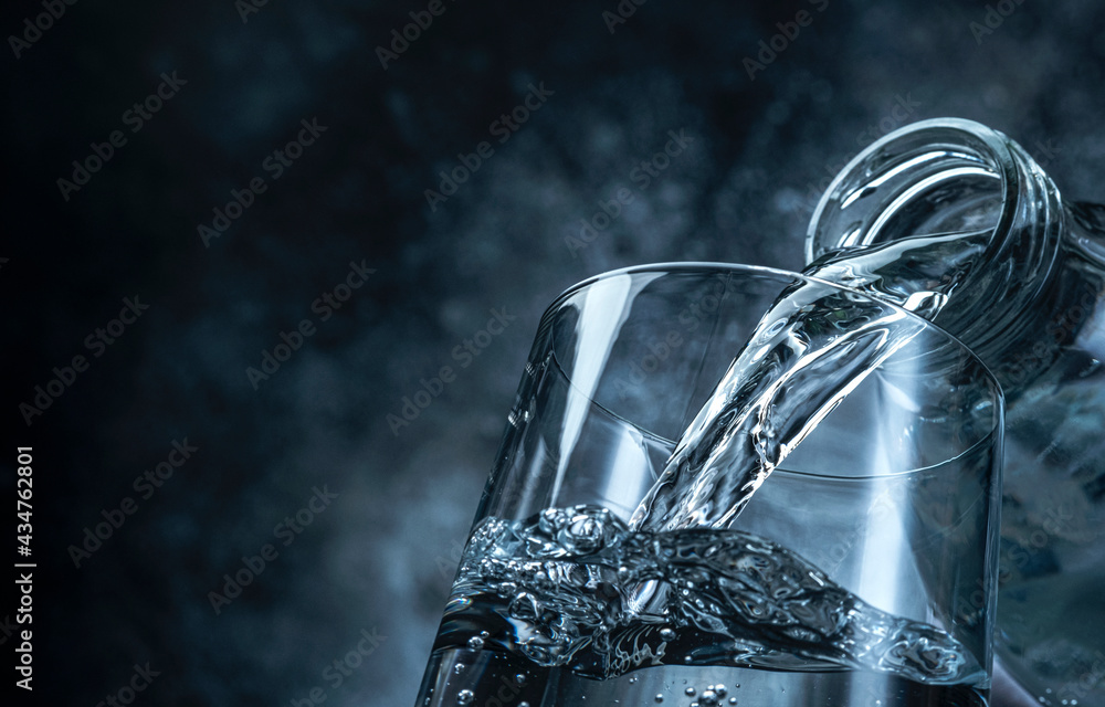 Pouring water from bottle into glass on black background