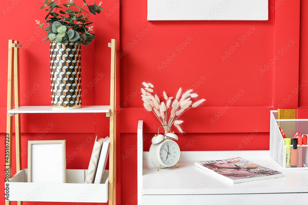 Book shelf and table with alarm clock near color wall