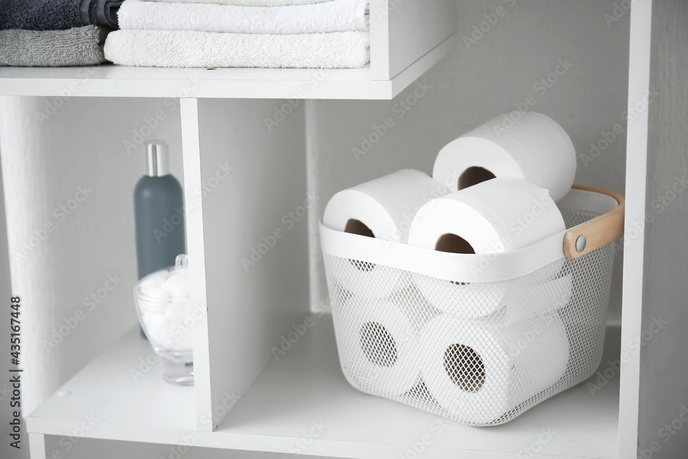 Shelf with rolls of toilet paper and bath supplies in bathroom