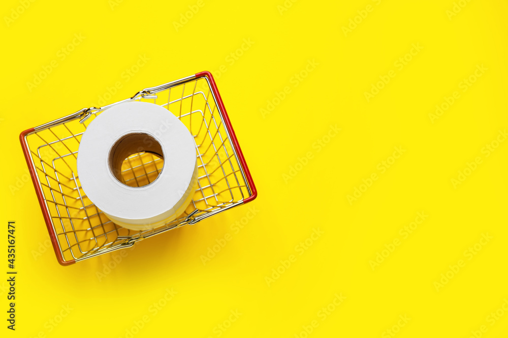 Shopping basket with roll of toilet paper on color background