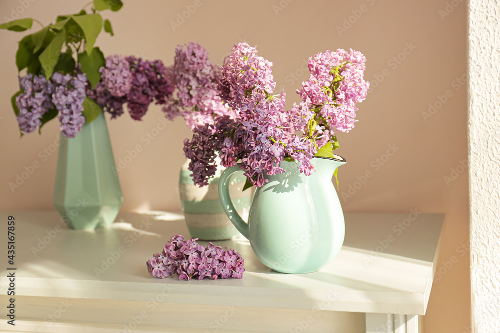 Vases with beautiful lilac flowers on table in room