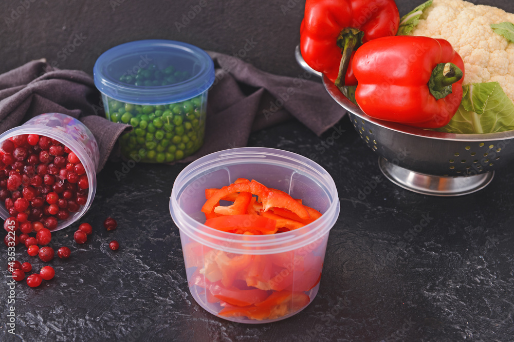 Plastic containers with vegetables and berries on dark background