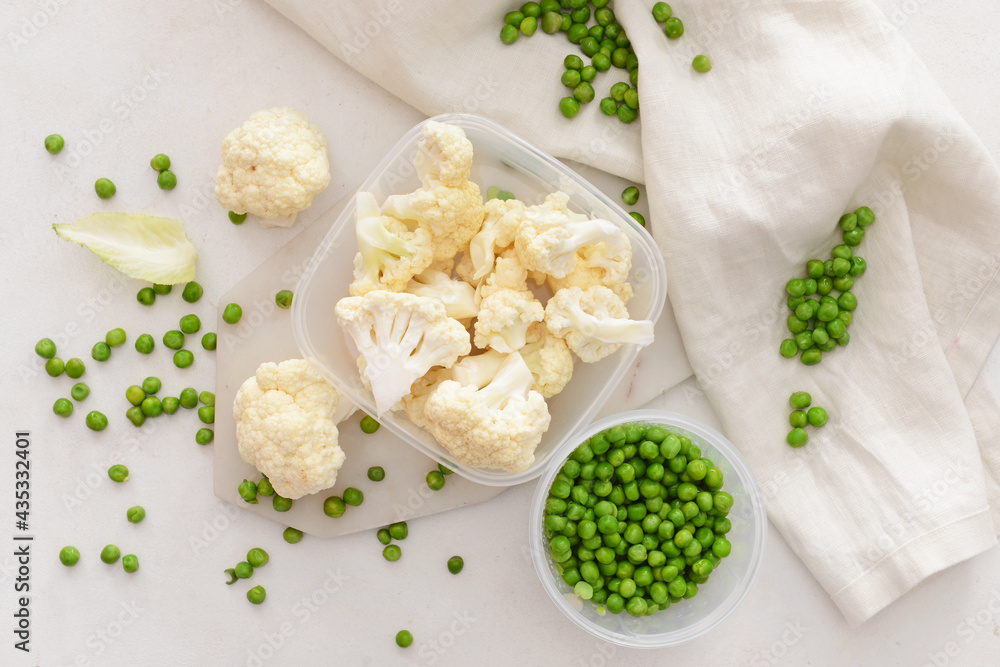 Plastic containers with green peas and cauliflower on light background