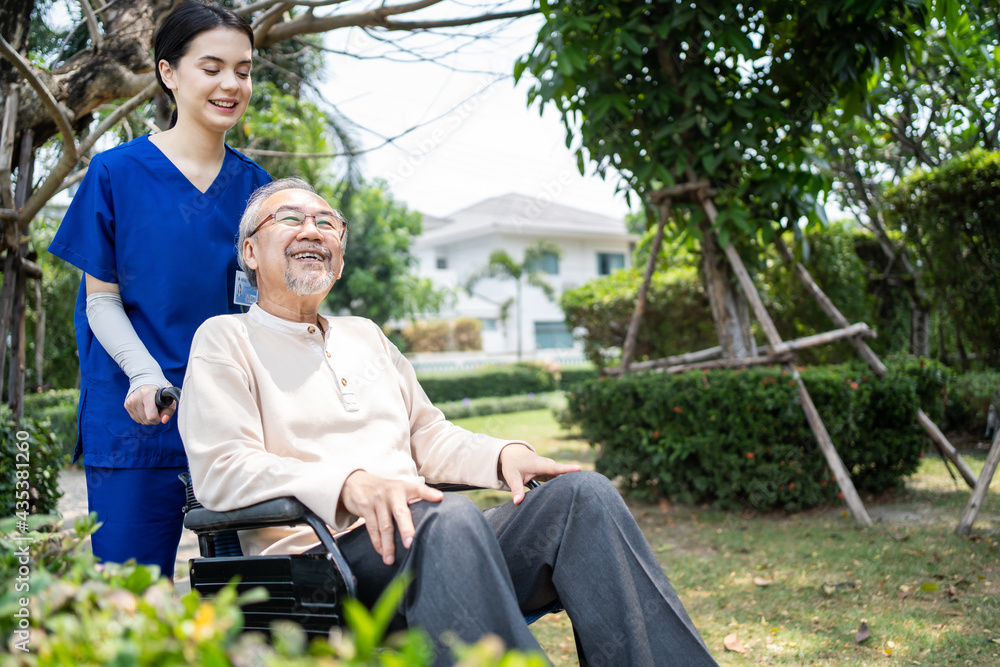 Asian female nurse pushing old man sit on wheelchair in public park