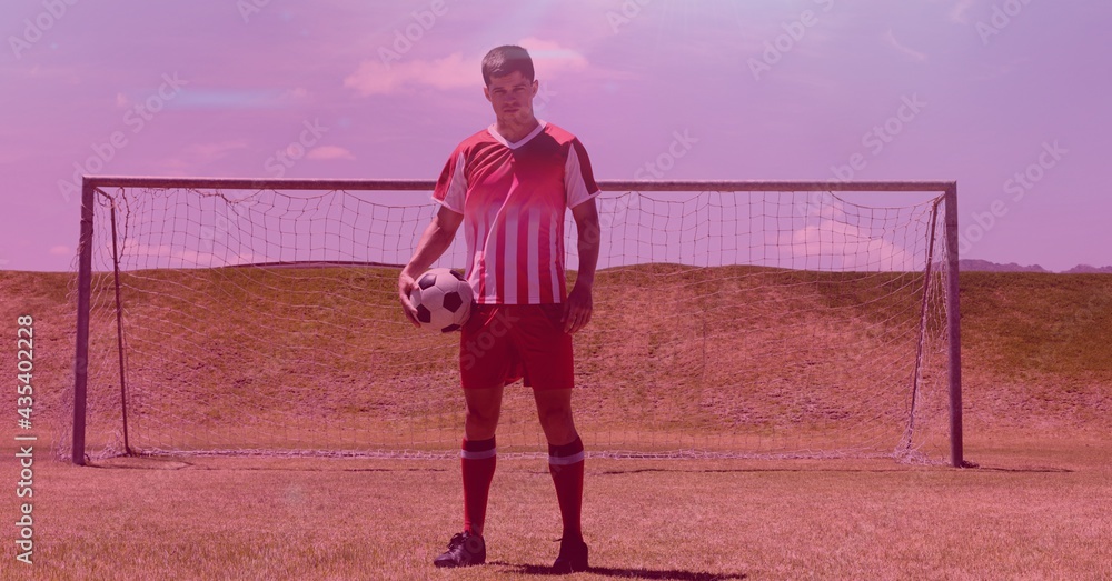 Composition of footballer holding ball on football pitch with pink background