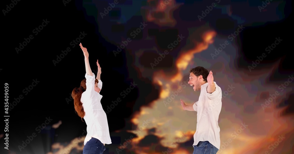 Composition of happy couple celebrating, smiling with arms outstretched, over dark cloudy suncet sky