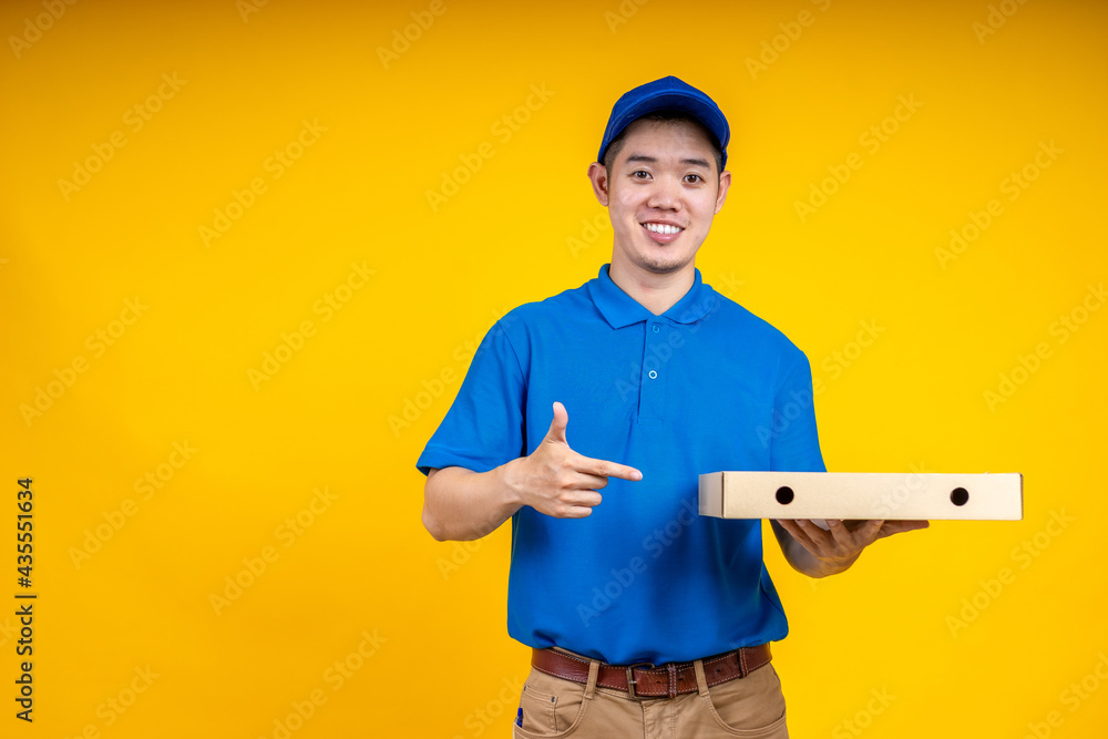 Young Asian handsome delivery man pointing to pizza boxs over yellow isolate background. Work from h