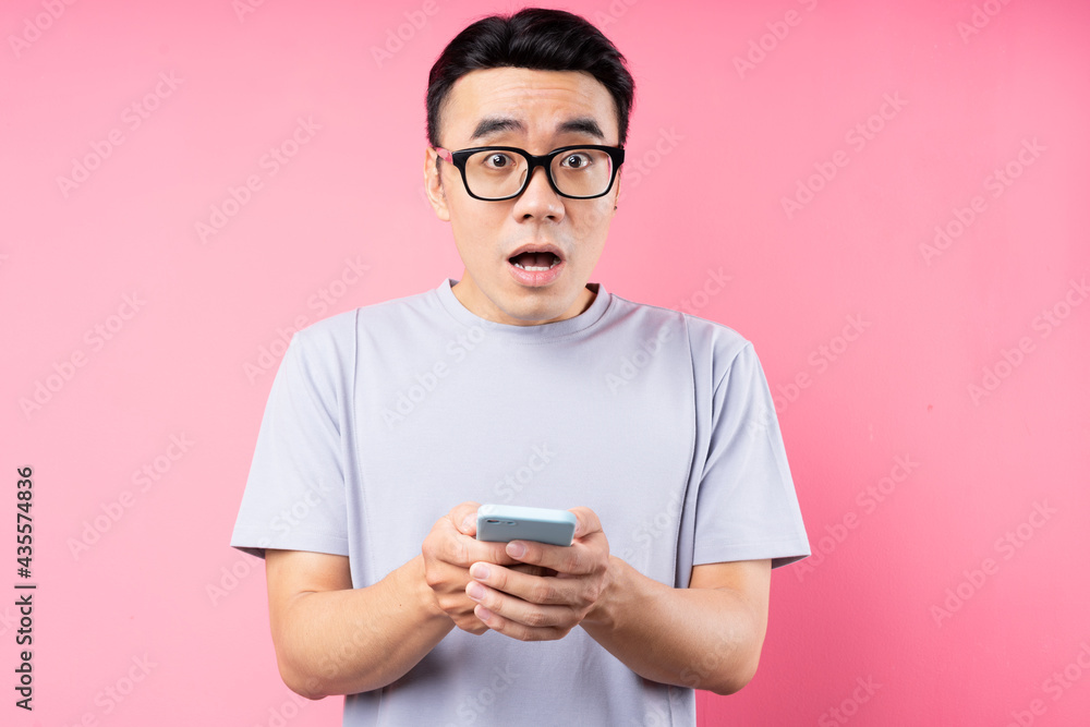 Portrait of Asian man using smartphone on pink background