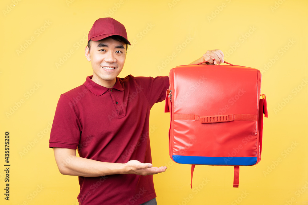 Asian delivery man wearing a red uniform posing on yellow background