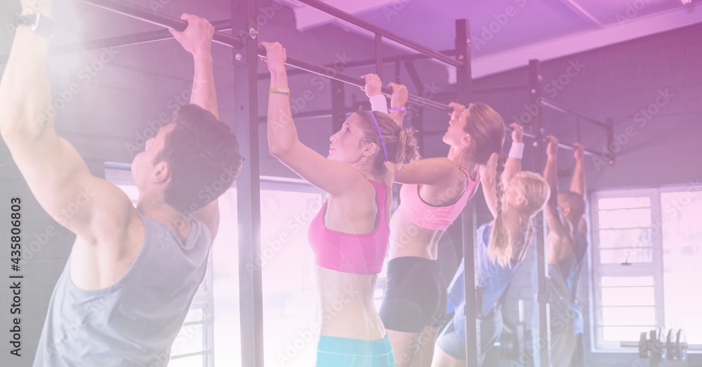 Strong women and man pulling up on bar exercising in gym with purple tinted background