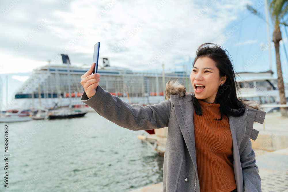 asian female traveller hand hold smartphone taking photo of cruise ship near cruise port with clear 