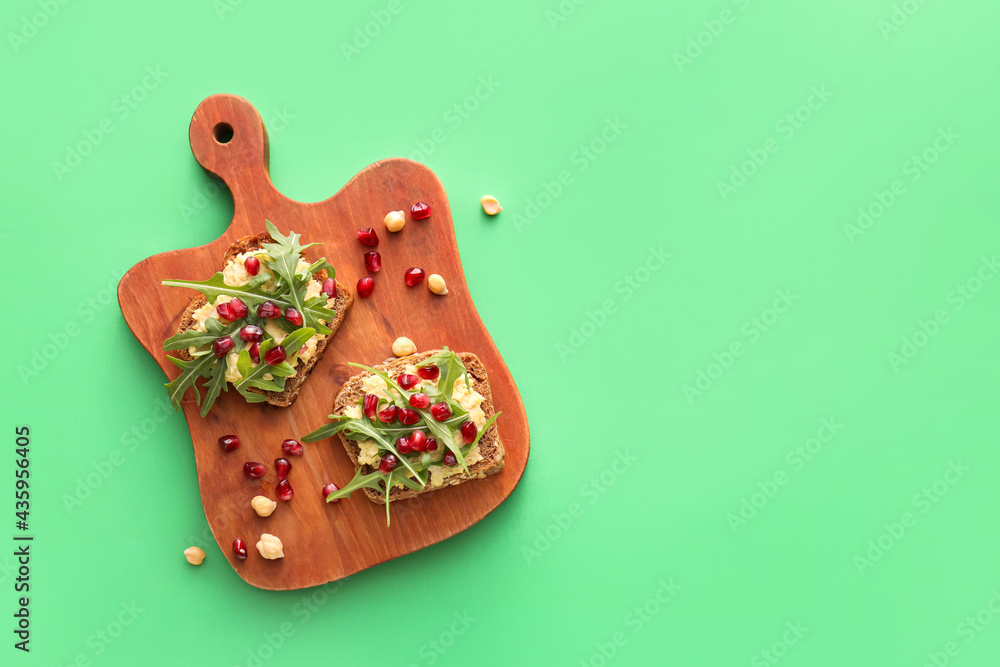 Tasty bruschettas with pomegranate and hummus on color background