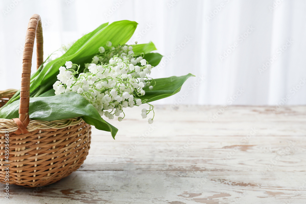 Basket with beautiful lily-of-the-valley flowers on light wooden background