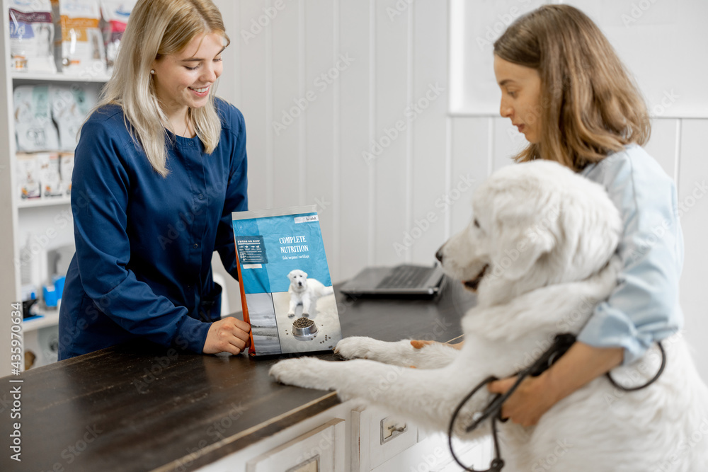 Female owner with big white dog on reception in veterinary clinic choosing dry food for the pet. Dog