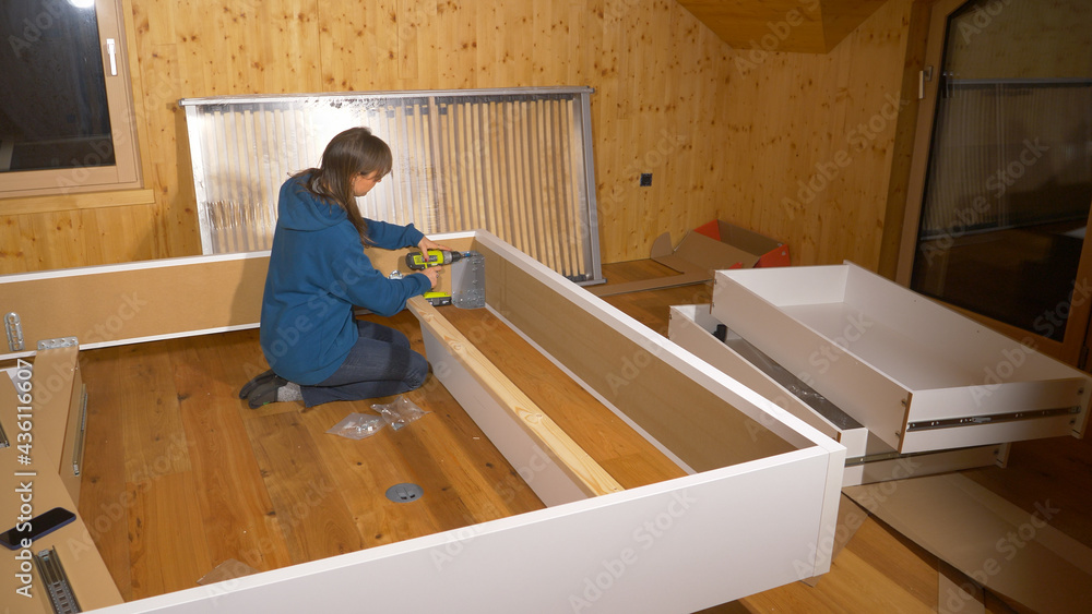 CLOSE UP: Young woman screws together the bed frame in unfinished bedroom.