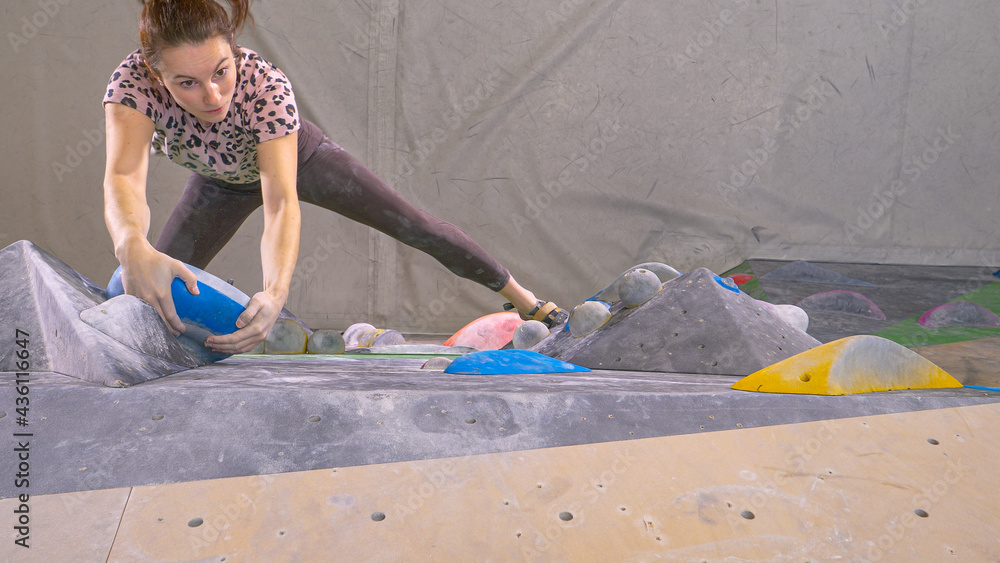 TOP DOWN: Caucasian woman climbs towards the top of an indoor bouldering wall.