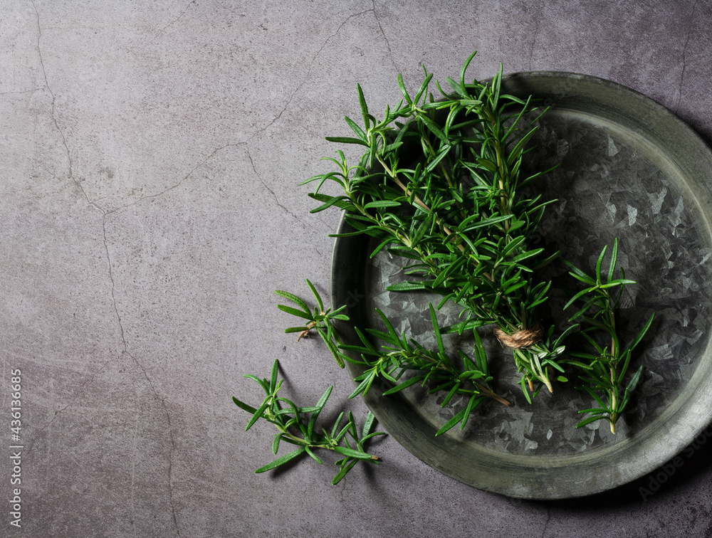 A bunch of fresh rosemary on an iron plate set against a dark background.