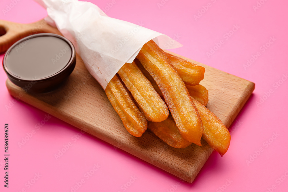 Board with tasty churros and melted chocolate sauce on color background