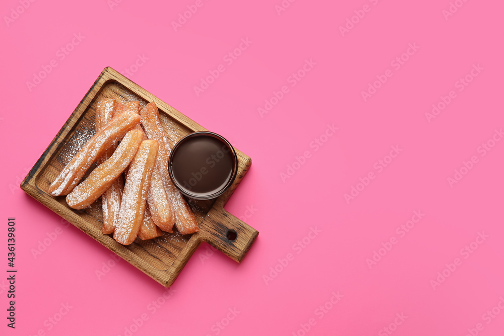 Board with tasty churros and melted chocolate sauce on color background