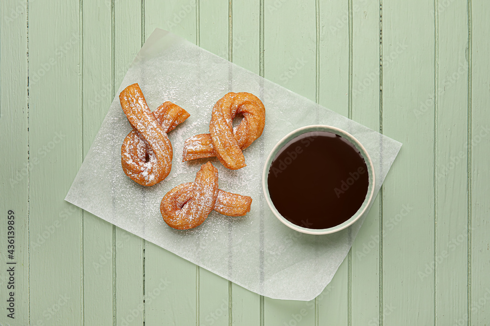 Parchment with tasty churros and melted chocolate sauce on color wooden background