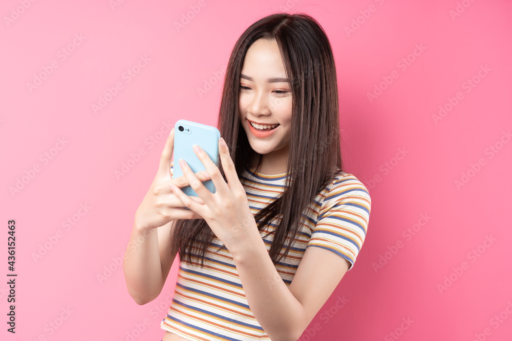 Young Asian woman using smartphone on pink background